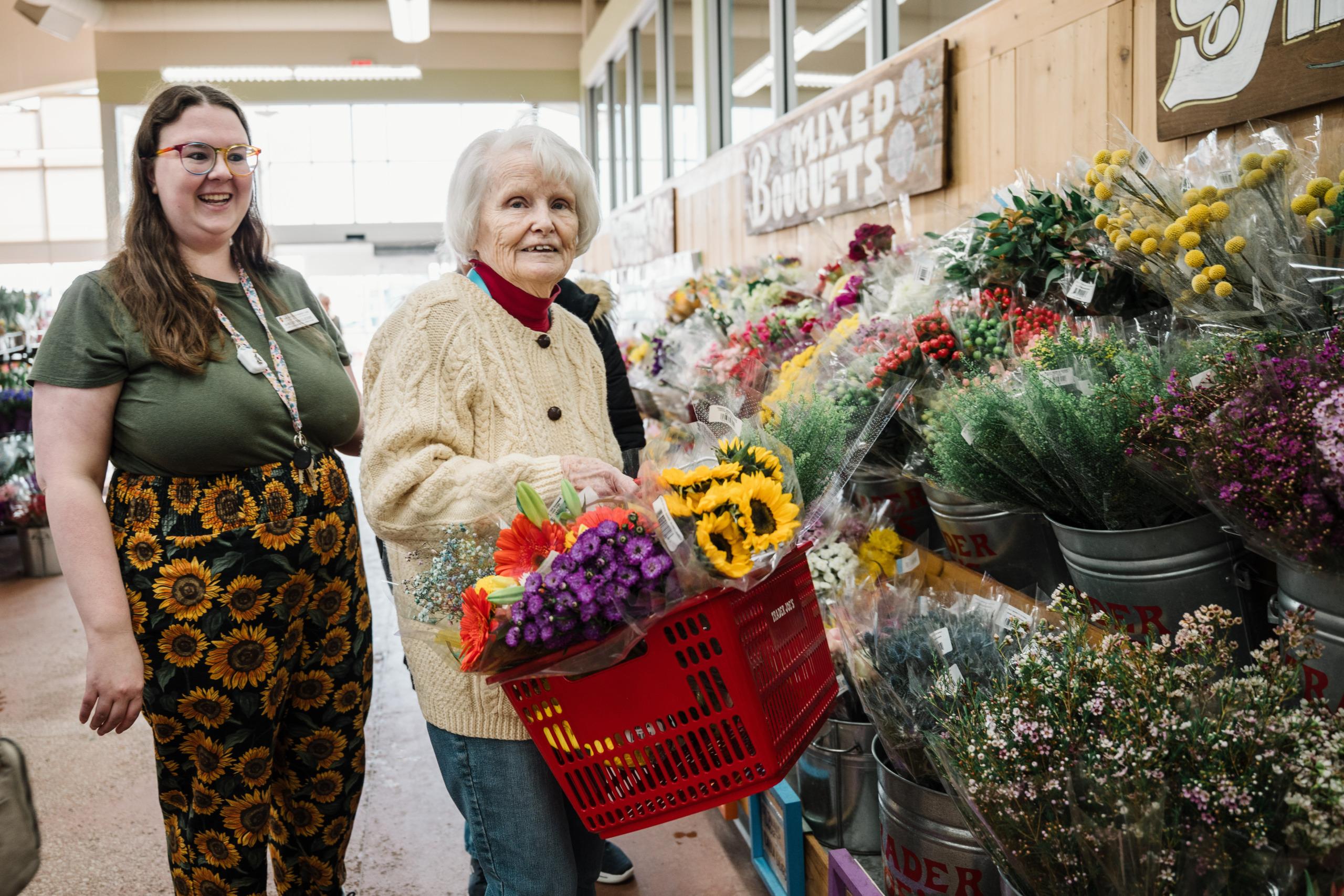 A resident and team member are buying flowers for flower arranging. The resident is holding a basket filled with beautiful flowers.