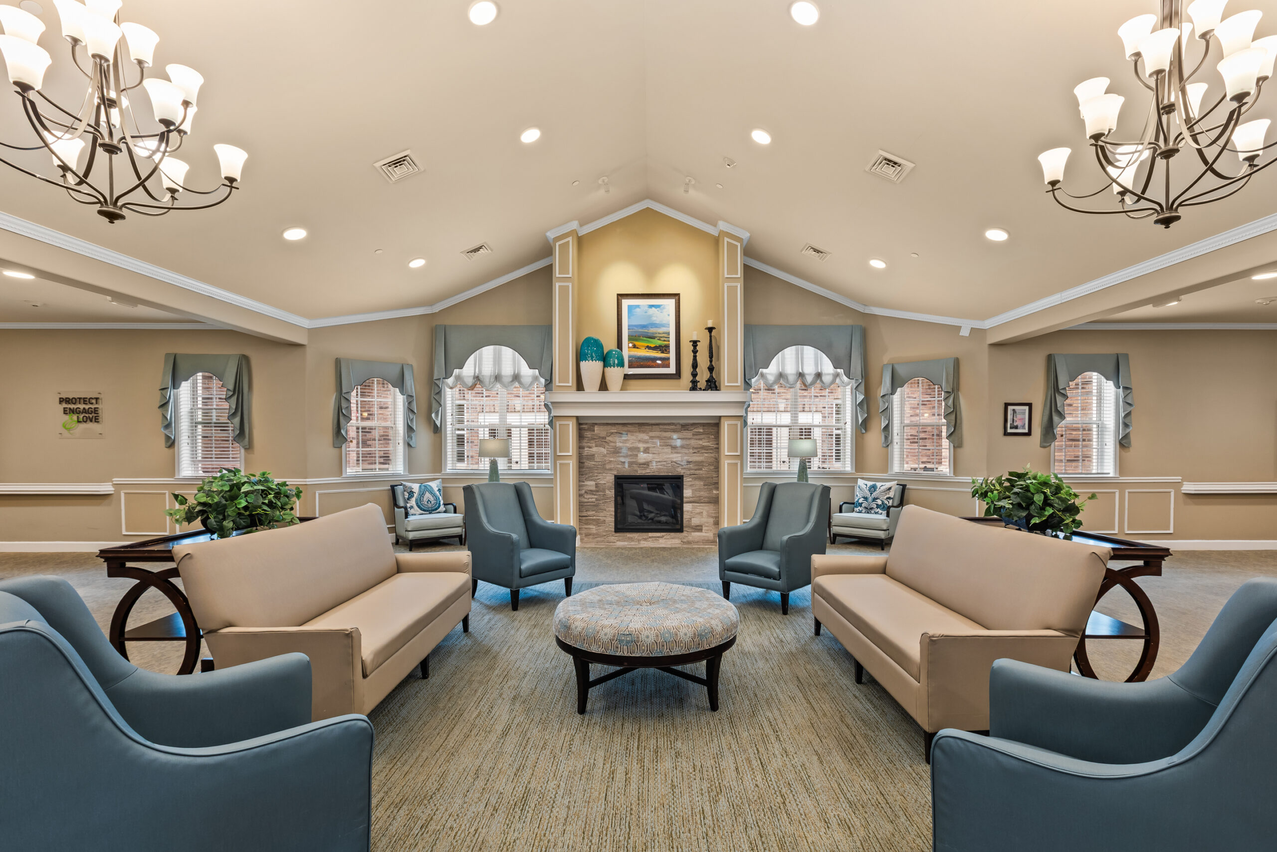 A spacious, symmetrical common lounge area with vaulted ceilings, featuring four distinct seating areas focused around a stone fireplace with a mantle.