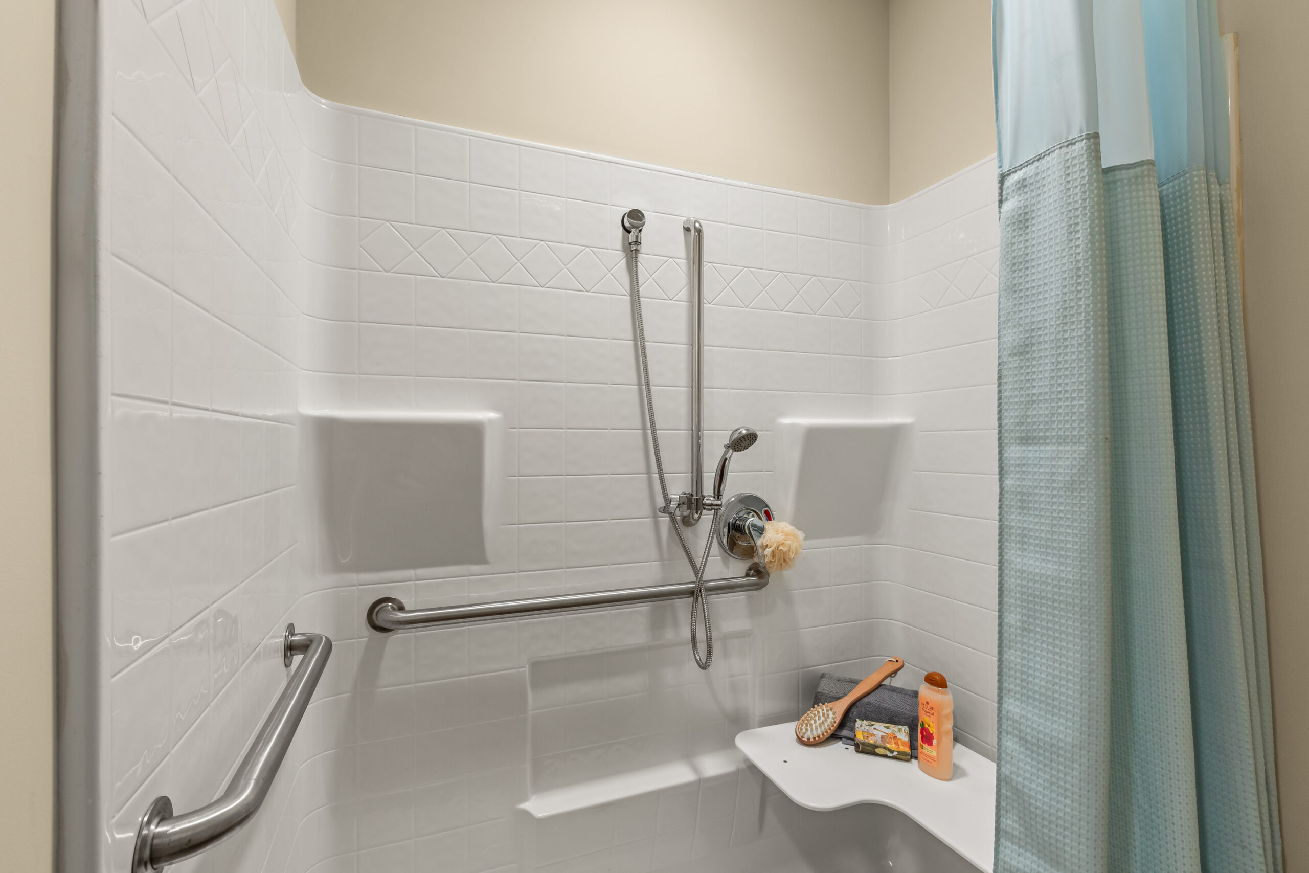 A model unit bedroom with an olive green accent wall behind a dark wood bed, a large window with white blinds, and a blue throw blanket over white bedding.